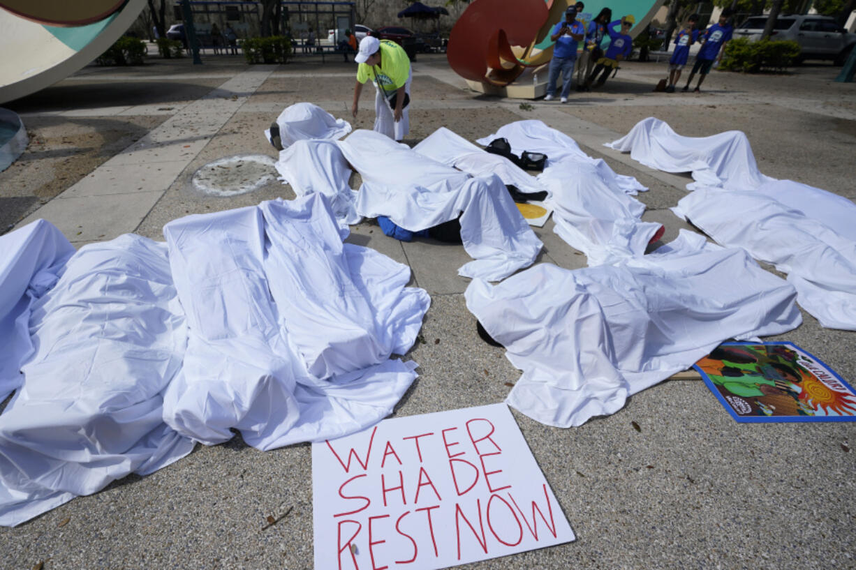 FILE - Demonstrators cover themselves with sheets to simulate workers killed by extreme heat, June 21, 2023, during a rally by outdoor workers demanding workplace protections against extreme heat, at the Stephen P. Clark Government Center in Miami.