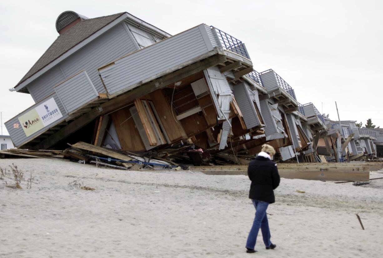 FILE - A woman walks past a cabana complex on the beach pulled off its foundations by Superstorm Sandy in Sea Bright, N.J., Nov. 19, 2012.