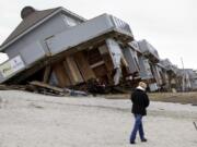 FILE - A woman walks past a cabana complex on the beach pulled off its foundations by Superstorm Sandy in Sea Bright, N.J., Nov. 19, 2012.