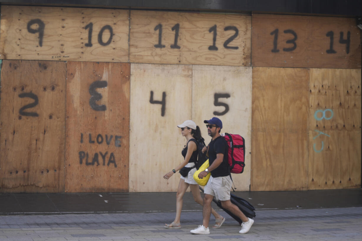 FILE - People walk past a souvenir shop&rsquo;s storefront boarded up preparation for the arrival of Hurricane Beryl, in Playa del Carmen, Mexico, July 4, 2024.