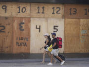 FILE - People walk past a souvenir shop&rsquo;s storefront boarded up preparation for the arrival of Hurricane Beryl, in Playa del Carmen, Mexico, July 4, 2024.