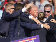 Republican presidential candidate former President Donald Trump is surrounded by U.S. Secret Service agents as he is helped off the stage at a campaign rally in Butler, Pa., Saturday, July 13, 2024. (AP Photo/Gene J.