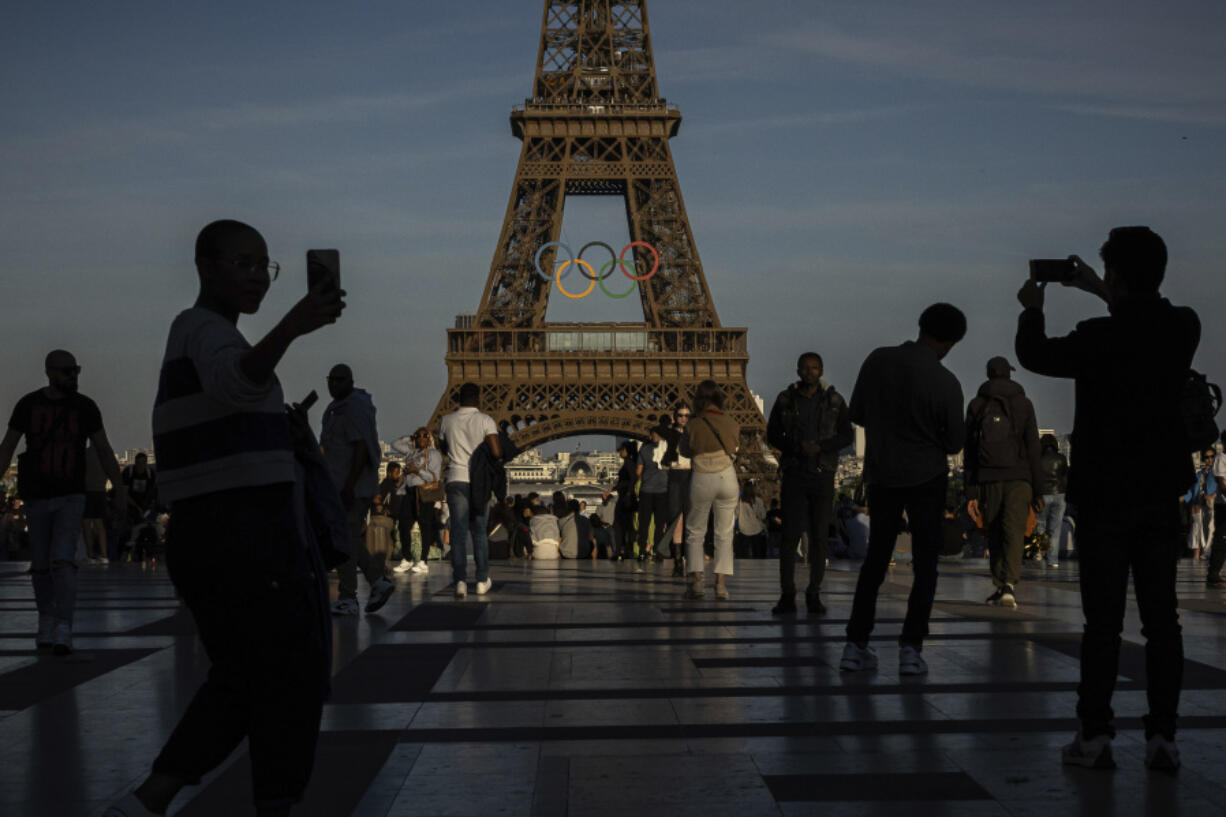 FILE - People use their smartphones near the Olympic rings that are displayed on the Eiffel Tower in Paris, June 7, 2024 in Paris. Cybersecurity experts and French officials say Russian disinformation campaigns against France are zeroing in on legislative elections and the Olympic Games which open in Paris at the end of the month.