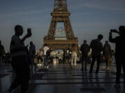 FILE - People use their smartphones near the Olympic rings that are displayed on the Eiffel Tower in Paris, June 7, 2024 in Paris. Cybersecurity experts and French officials say Russian disinformation campaigns against France are zeroing in on legislative elections and the Olympic Games which open in Paris at the end of the month.