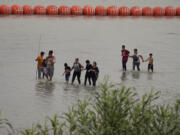 FILE - Migrants who crossed the Rio Grande from Mexico walk past large buoys being deployed as a border barrier on the river in Eagle Pass, Texas, July 12, 2023. The floating barrier is being deployed in an effort to block migrants from entering Texas from Mexico.