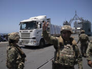 A U.S. Army soldier gestures as trucks loaded with humanitarian aid arrive at the U.S.-built floating pier Trident before reaching the beach on the coast of the Gaza Strip, Tuesday, June 25, 2024.