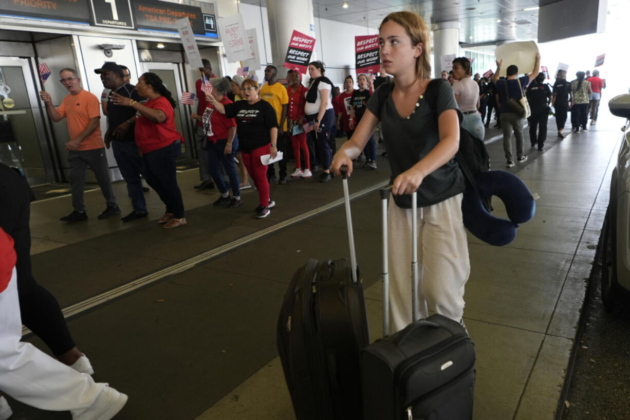 A traveler walks through the departure area as airline catering workers who are employed by Gate Gourmet picket with their supporters, calling for a new union contract with raises and affordable health insurance, Wednesday, July 3, 2024, at Miami International Airport in Miami. A long Fourth of July holiday weekend is expected to create new travel records.