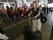 A traveler walks through the departure area as airline catering workers who are employed by Gate Gourmet picket with their supporters, calling for a new union contract with raises and affordable health insurance, Wednesday, July 3, 2024, at Miami International Airport in Miami. A long Fourth of July holiday weekend is expected to create new travel records.