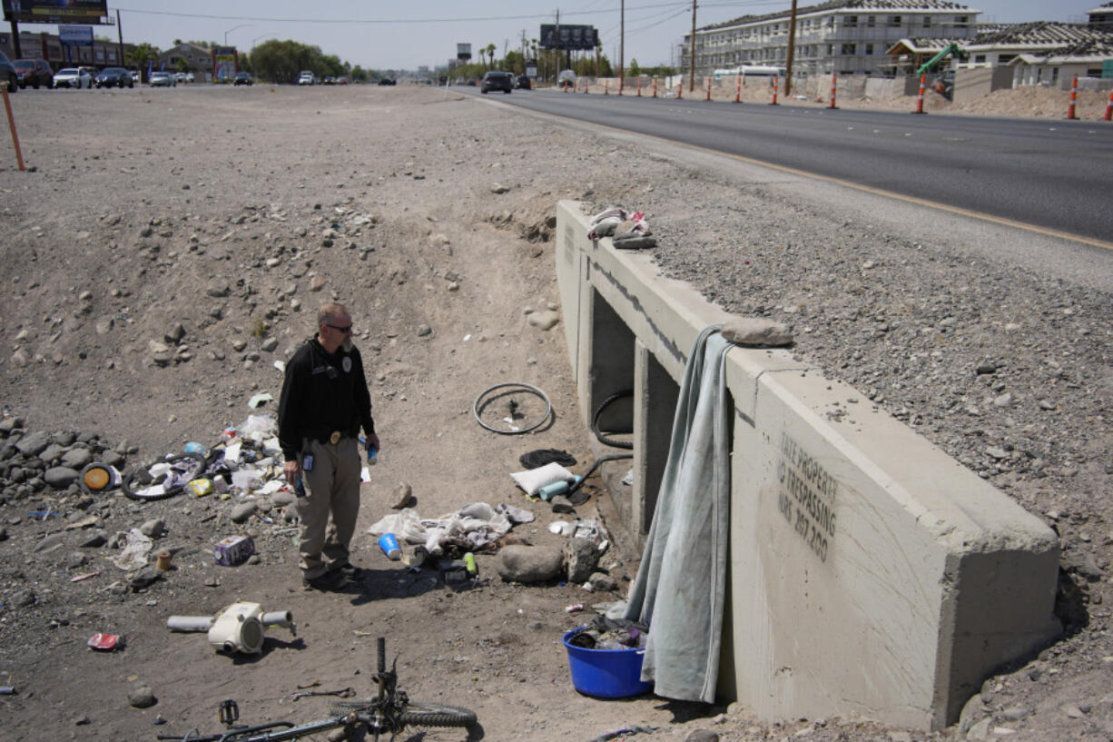 Mark Paulson, a Public Response and Code Enforcement officer, holds cans of cold water while checking on a homeless encampment, Wednesday, July 10, 2024, in Henderson, Nev. About 14 officers from the Office of Public Response drove around the city Wednesday offering water, electrolytes, free bus tickets and rides to cooling centers during a heat emergency.