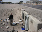 Mark Paulson, a Public Response and Code Enforcement officer, holds cans of cold water while checking on a homeless encampment, Wednesday, July 10, 2024, in Henderson, Nev. About 14 officers from the Office of Public Response drove around the city Wednesday offering water, electrolytes, free bus tickets and rides to cooling centers during a heat emergency.