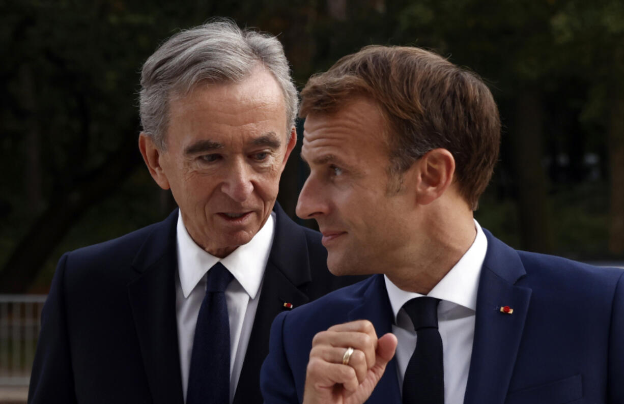 FILE - LVMH luxury group CEO Bernard Arnault, left, and French President Emmanuel Macron arrive at Fondation Louis Vuitton to visit the exhibition &lsquo;The Morozov Collection, Icons of Modern Art&rsquo; in Paris, Tuesday, Sept. 21, 2021. With a major sponsorship role aimed at burnishing the image of the Paris 2024 Summer Olympic Games and the French capital, it&rsquo;s a new chapter in LVMH&rsquo;s specialty of selling exclusivity at a grand scale under its chair and CEO, Arnault.