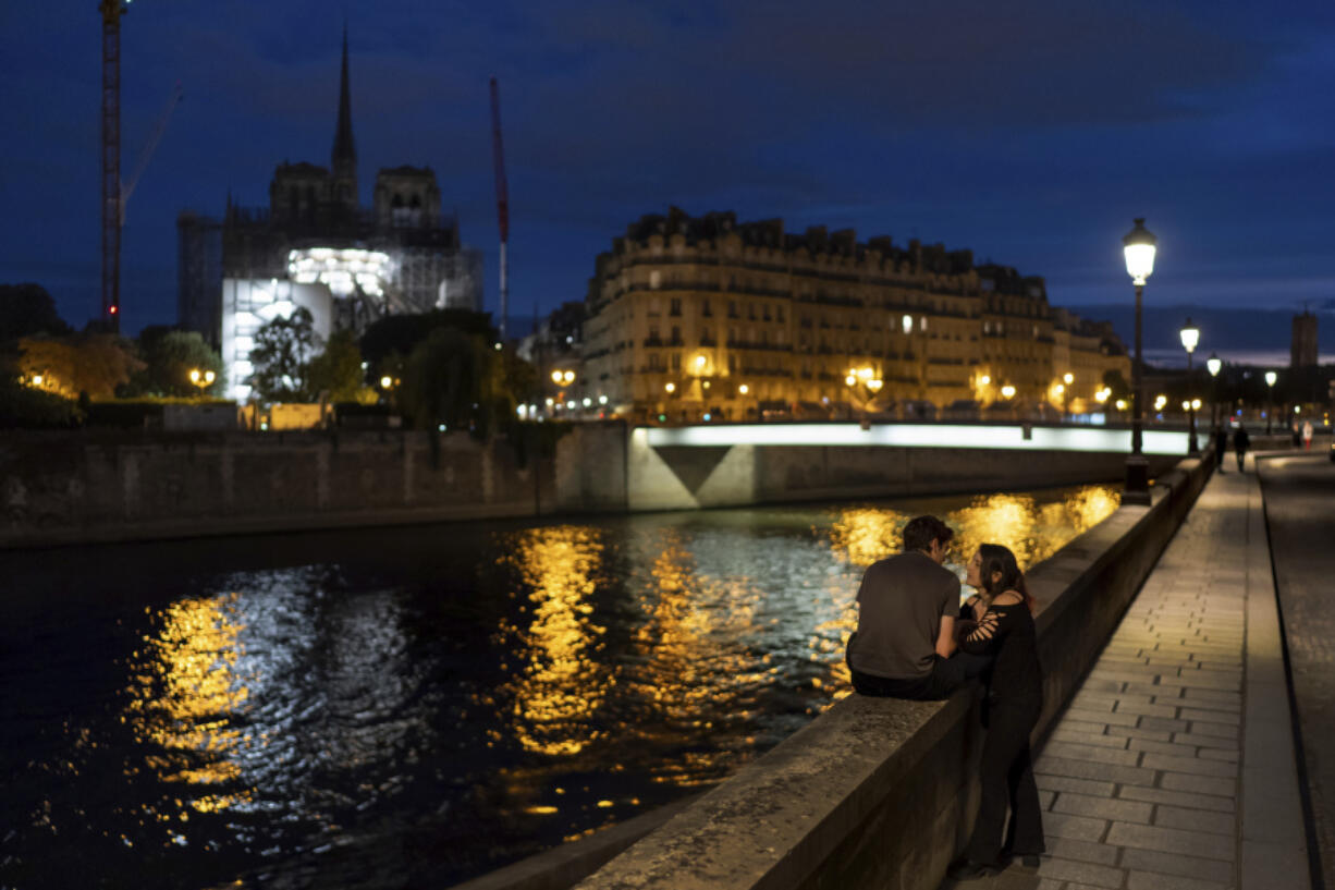 Victor, left, and his girlfriend, Florence, talk along the Seine River at dusk as the spire of the Notre Dame Cathedral rises in the background ahead of the 2024 Summer Olympics, Tuesday, July 16, 2024, in Paris, France.