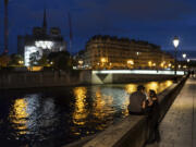 Victor, left, and his girlfriend, Florence, talk along the Seine River at dusk as the spire of the Notre Dame Cathedral rises in the background ahead of the 2024 Summer Olympics, Tuesday, July 16, 2024, in Paris, France.