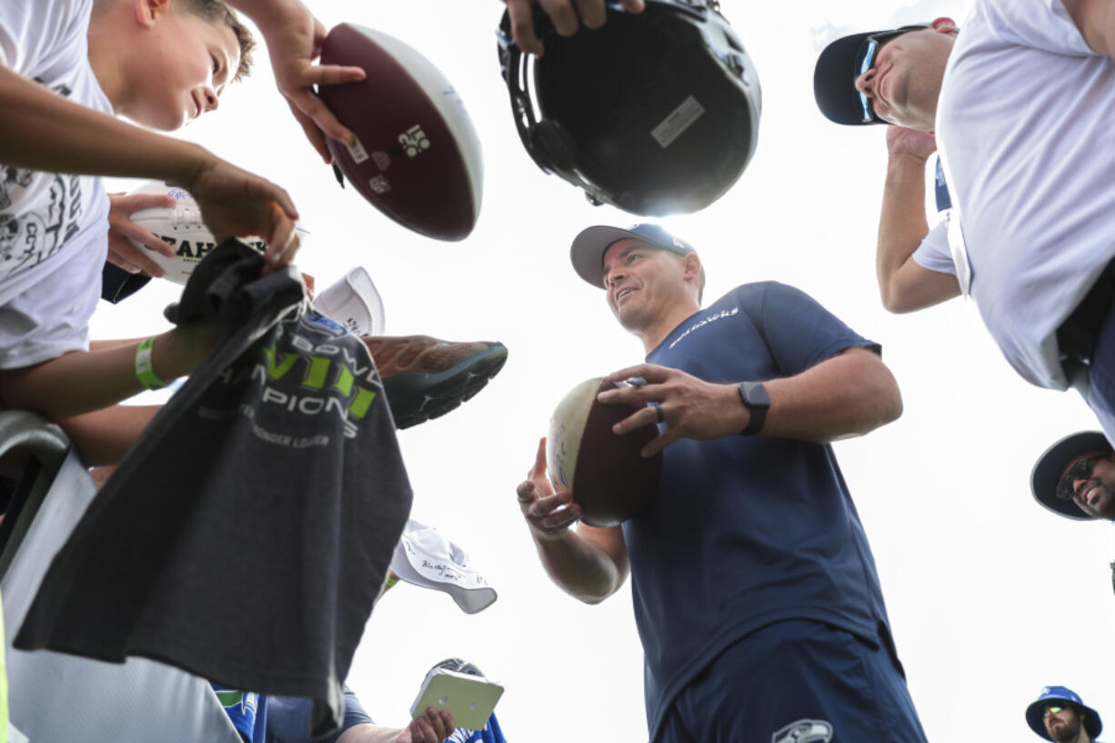 Seattle Seahawks head coach Mike Macdonald, center, signs autographs following NFL football training camp in Renton, Wash., Wednesday, July 24, 2024.