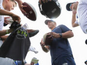 Seattle Seahawks head coach Mike Macdonald, center, signs autographs following NFL football training camp in Renton, Wash., Wednesday, July 24, 2024.