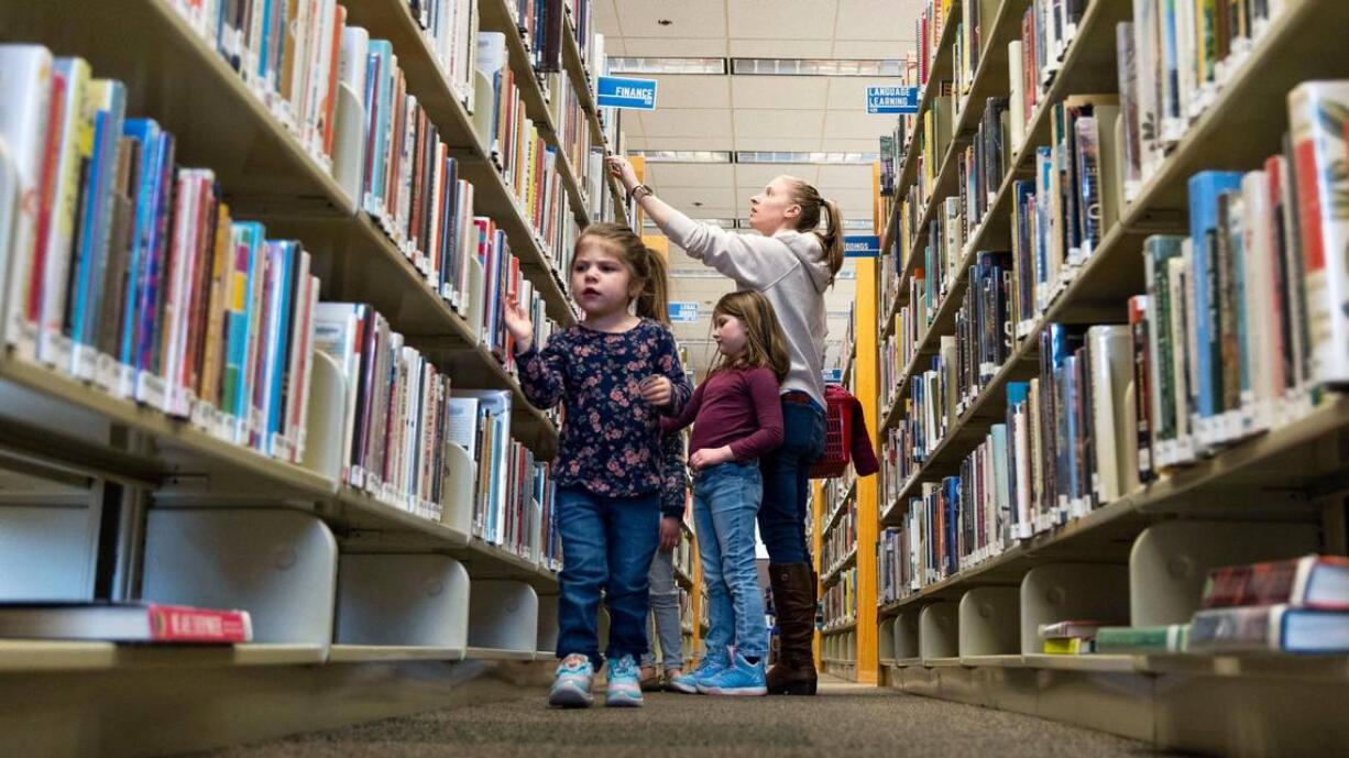 Four-year-old Makenna Kitzmiller walks along a row of books as her mother, Rachel Kitzmiller, looks for a book title last month at the Meridian Library on Cherry Lane with her children, Claire, 7, and Andrea, 5.