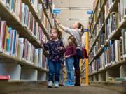 Four-year-old Makenna Kitzmiller walks along a row of books as her mother, Rachel Kitzmiller, looks for a book title last month at the Meridian Library on Cherry Lane with her children, Claire, 7, and Andrea, 5.