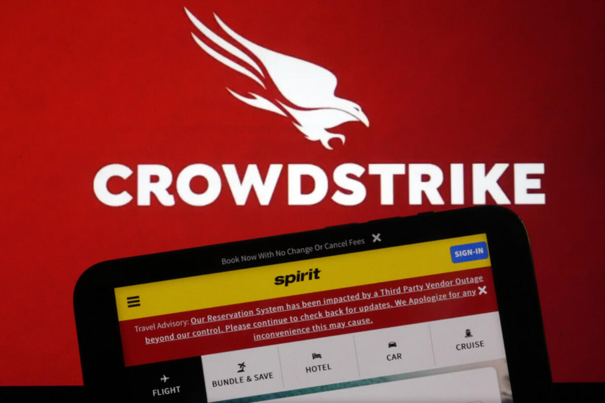 The logo for CrowdStrike and a Spirit Airlines webpage are shown on a computer screen and mobile phone screen, in New York, Friday, July 19, 2024. A global technology outage grounded flights, knocked banks offline and media outlets off air after a faulty software update disrupted companies and services around the world and highlighted their dependence on just a handful of providers.