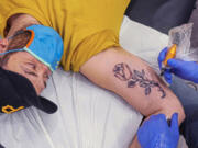 Eric Mallinger watches while Richard Lattanzi tattoos a rose on his arm at the JCC in Pittsburgh. The rose is in honor of his grandmother, Rose Mallinger, one of 11 people killed while attending worship services at Tree of Life synagogue in 2018. The Food and Drug Administration has raised concerns about potentially dangerous bacteria in tattoo inks.