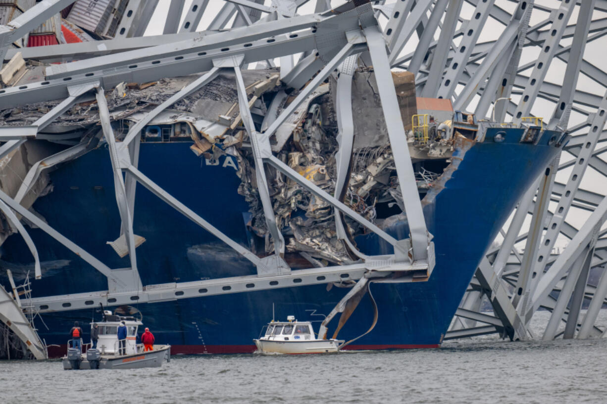 Boats are dwarfed by the twisted structure from the Francis Scott Key Bridge draped across the container ship Dali.