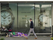 FILE - A person sleeps next to a shopping cart as a pedestrian walks past a store-window sign advertising the future opening of a Rolex watch store on Jan. 31, 2022, in downtown Seattle. In Feb. 2022, the mayor of Portland, Ore., banned camping on the sides of certain roadways, and officials are exploring other aggressive options to combat homelessness. In an increasing numbers of liberal cities like Portland, Seattle and New York, officials are cracking down on encampments after years of tolerating growing numbers of people living in tents. (AP Photo/Ted S.