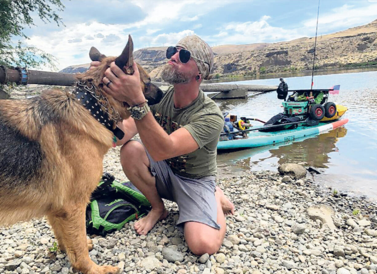 Michael Curtis of Washougal greets a dog along the Columbia River, in 2024. Curtis has raised more than $56,000 for Northwest Battle Buddies through his 1,000-mile journey down the Columbia River on a stand-up paddleboard.