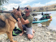 Michael Curtis of Washougal greets a dog along the Columbia River, in 2024. Curtis has raised more than $56,000 for Northwest Battle Buddies through his 1,000-mile journey down the Columbia River on a stand-up paddleboard.