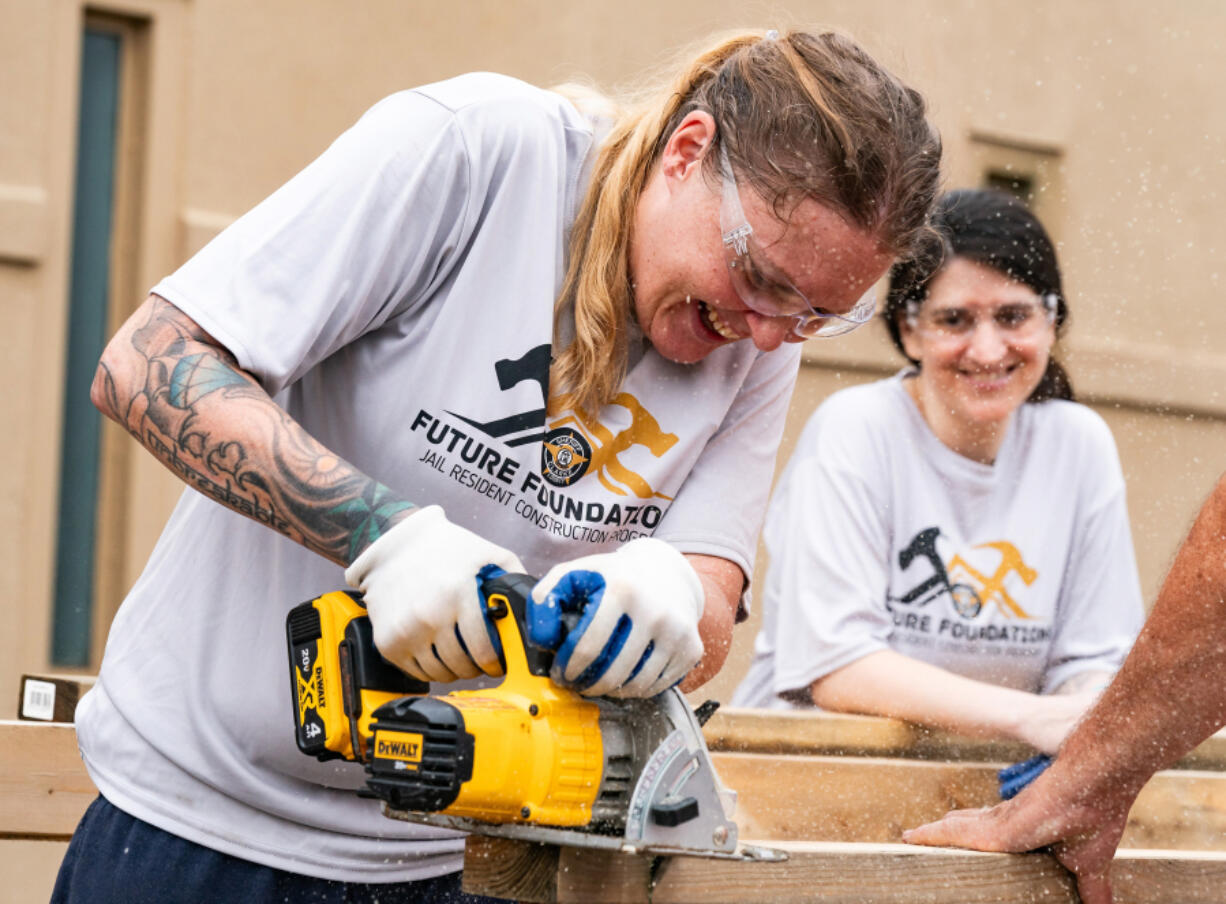 Nichole Mosley, an inmate at the Athens-Clarke County Jail, smiles as she saws through a piece of wood while building a tiny home in the jail yard in Athens, Georgia, on July 27, 2024.