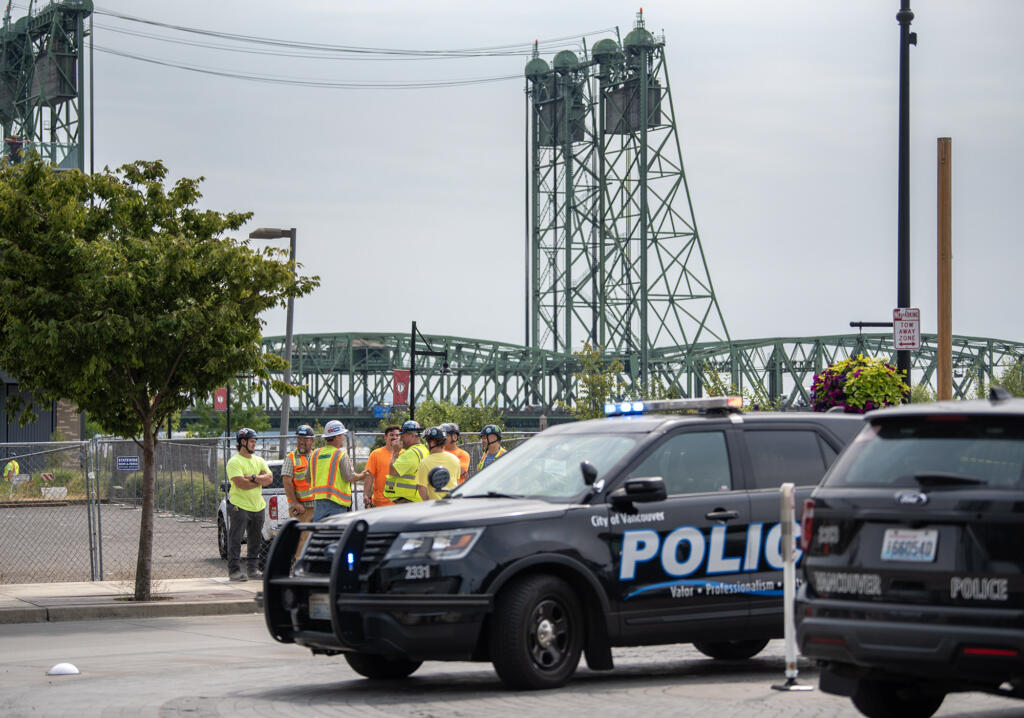 Construction workers stand near Vancouver Police vehicles Friday, Aug. 9, 2024, after being evacuated from their work sites due to a bomb threat in downtown Vancouver.