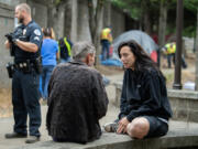 Cpl. Sean Metevia, left, looks on during a solid waste sweep of the sound wall along Mill Plain Boulevard as Tiffini Dillard, in black sweatshirt, of Vancouver&rsquo;s Homelessness Assistance and Resource Team listens to a camper.