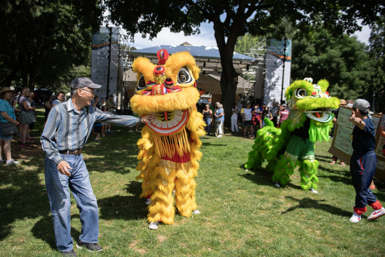 Vancouver resident Tom Nguyen, left, &ldquo;feeds&rdquo; a lion from the Vietnamese Community of Clark County on Friday during the Vancouver USA Arts &amp; Music Festival at Esther Short Park.