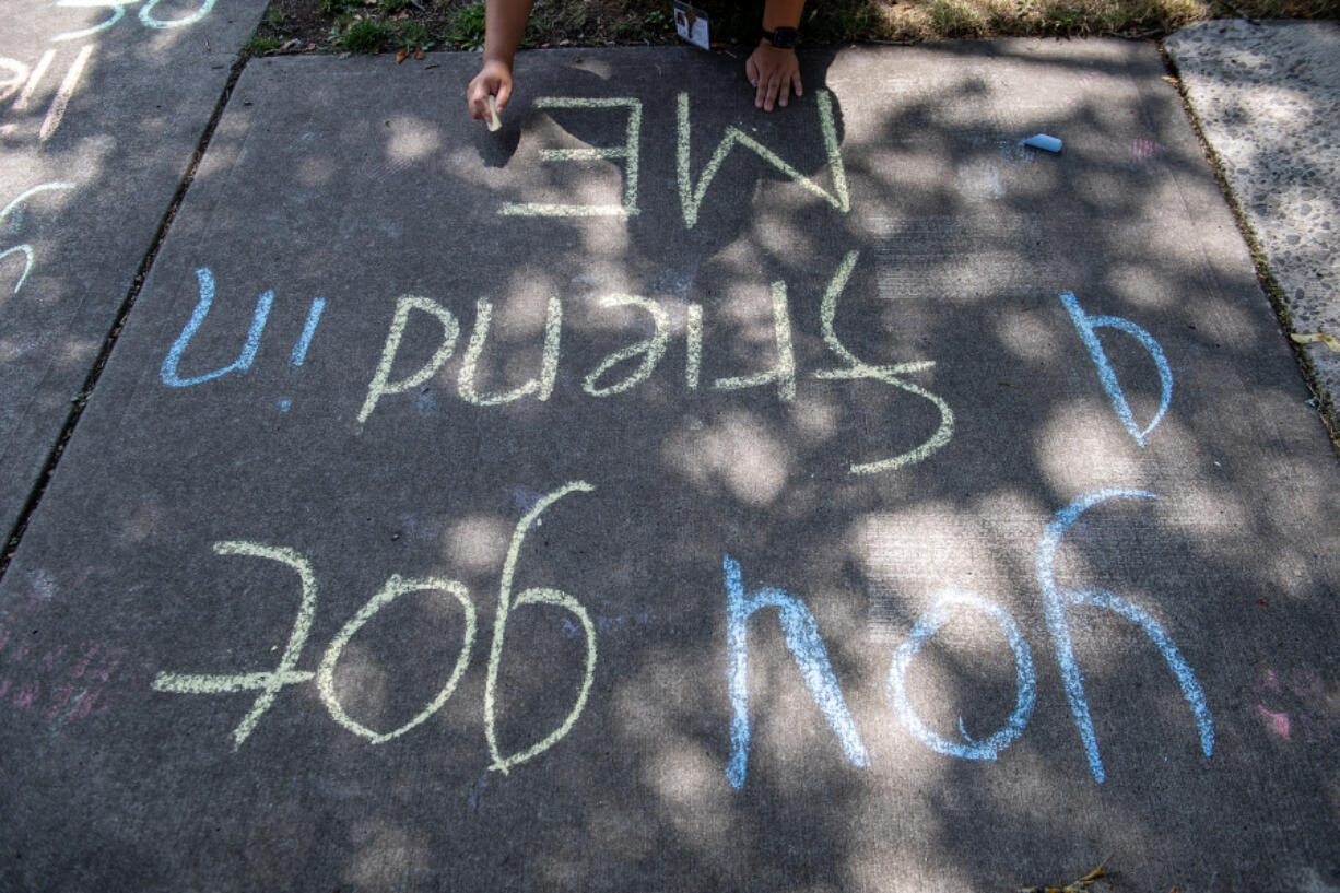 An intern writes a positive message in chalk outside the Clark County Juvenile Justice Center in Vancouver on Tuesday afternoon. .