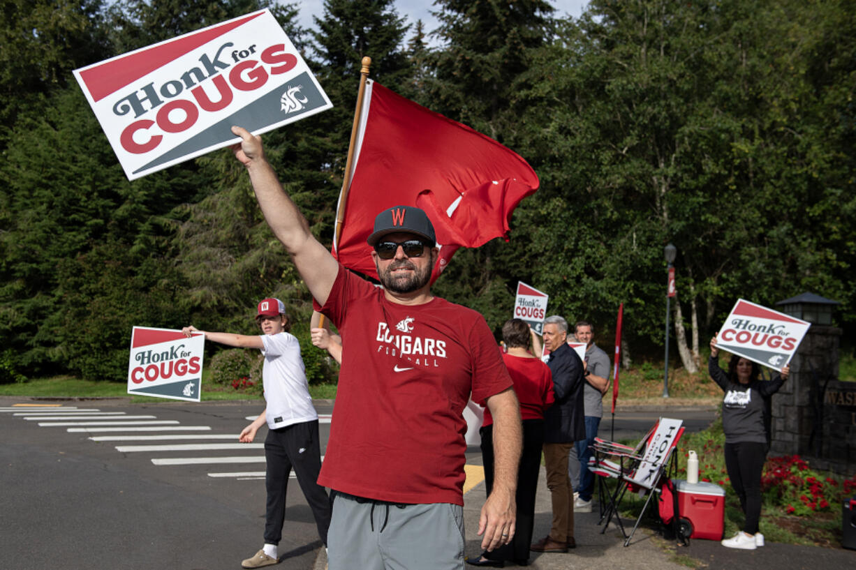 Washington State University fan Will Fisher, left, joins his dad, P.J. Fisher, who is a member of the class of 2003, and other supporters while greeting students on the first day of classes at Washington State University Vancouver on Monday morning.