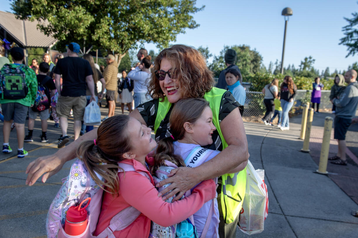 Second-grader Avery Harrington, 7, left, and her sister, third-grader Addison Harrington, 8, in purple, get a warm welcome from bilingual staff member Maria Vasquez, yellow vest, while arriving on the first day of school at Sarah J. Anderson Elementary School on Wednesday morning.