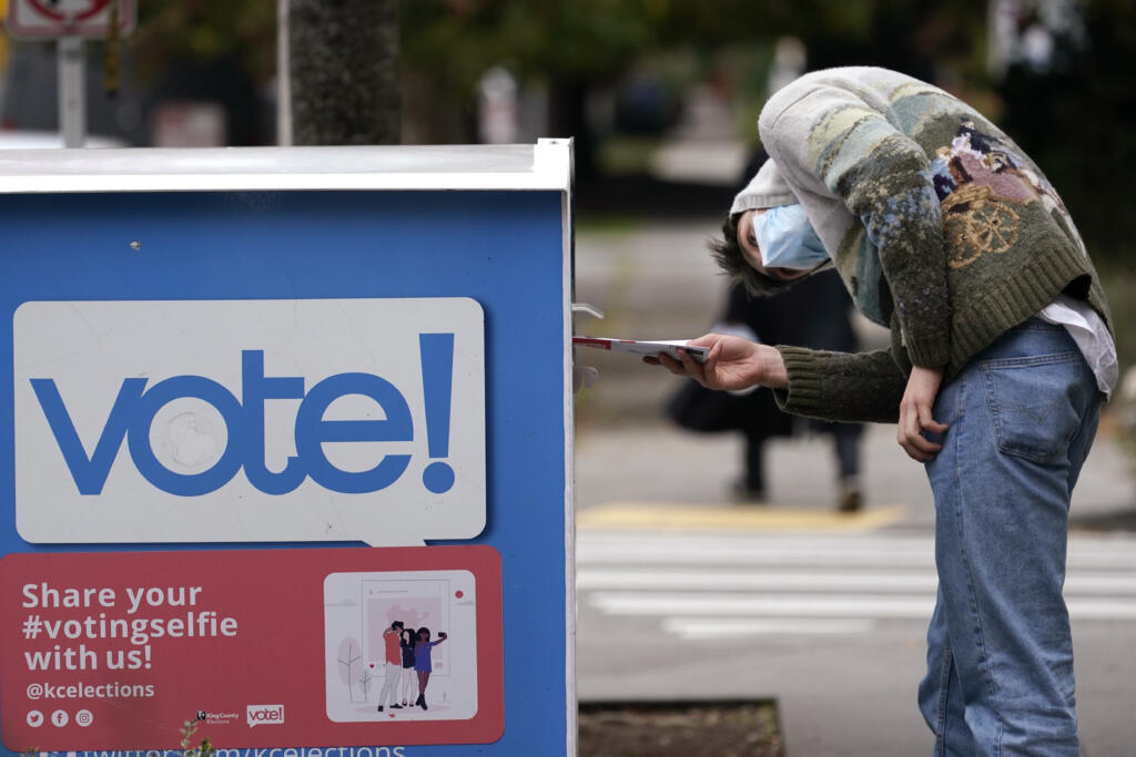 A voter turns sideways as he eyes the opening of a ballot drop box before placing his ballot inside it, Oct. 28, 2020, in Seattle. The Republican backers of three initiatives that could change important state policies are suing to keep each measure's fiscal impact from appearing on the November 2024 ballot, but lawyers for the state say the budget implications must be disclosed to voters.