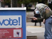 A voter turns sideways as he eyes the opening of a ballot drop box before placing his ballot inside it, Oct. 28, 2020, in Seattle. The Republican backers of three initiatives that could change important state policies are suing to keep each measure's fiscal impact from appearing on the November 2024 ballot, but lawyers for the state say the budget implications must be disclosed to voters.