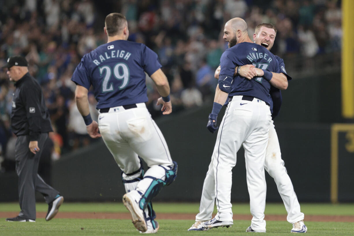 Seattle Mariners outfielder Mitch Haniger, center, is mobbed by Luke Raley, right, and Cal Raleigh (29) after Hanger's three-RBI, walk-off double during the ninth inning of a baseball game against the Detroit Tigers, Thursday, Aug. 8, 2024, in Seattle. The Mariners won 4-3.