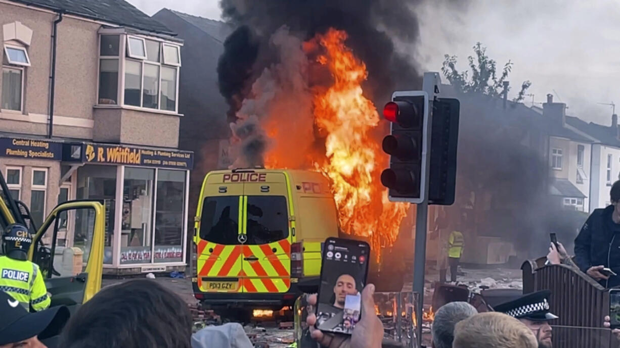 A police van buns as and unruly crowd clashed with police, Tuesday, July 30, 2024, in Southport, northwest England, near where three girls were stabbed to death in a dance class the day before. The violence erupted shortly after a peaceful vigil was attended by hundreds in the center of Southport to mourn the 13 victims of the stabbings, including seven still in critical condition.