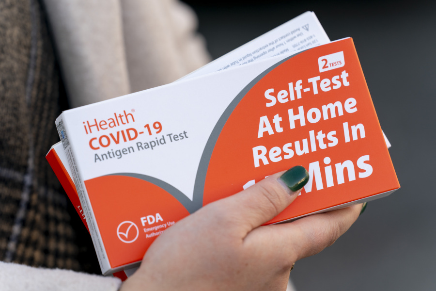 FILE - A woman holds two boxes of at-home Covid-19 test kits in Washington, Dec. 22, 2021.