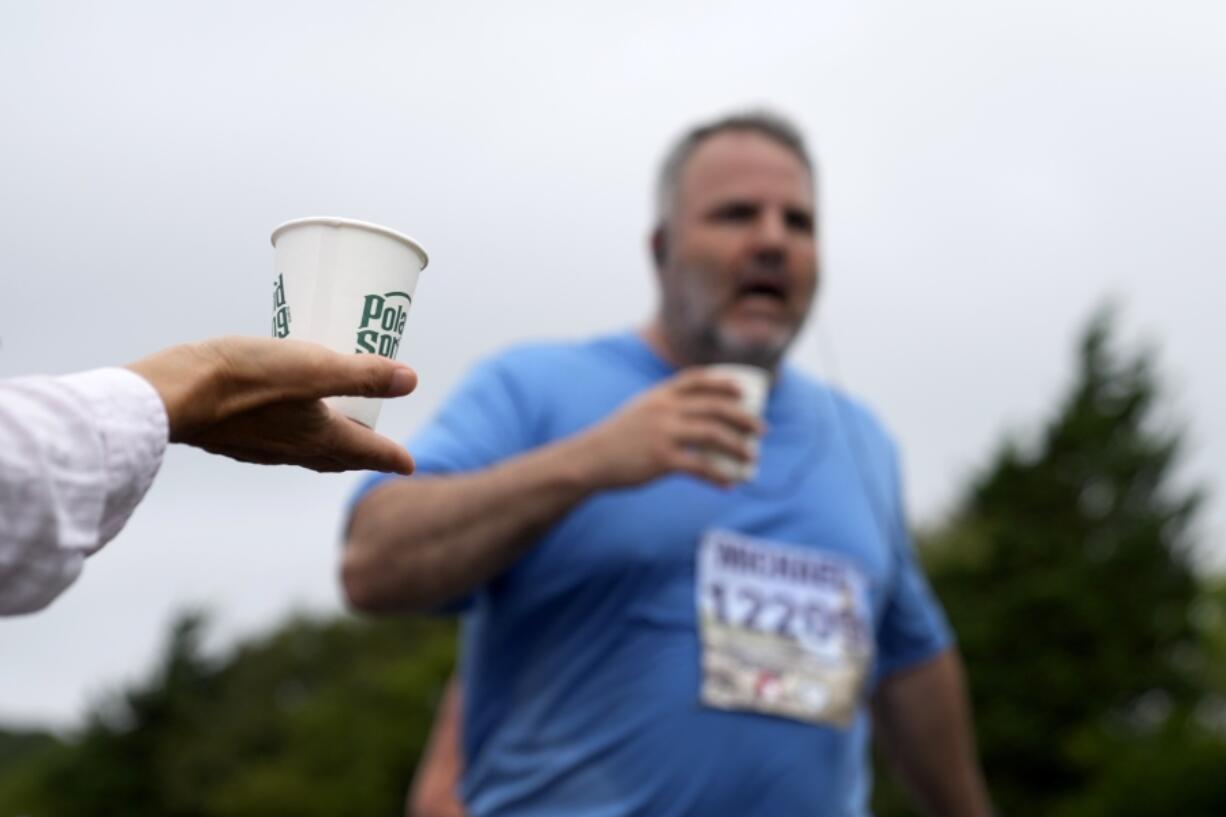 A volunteer holds out a cup of water for passing runners Aug. 18 at the 3-mile mark of the Falmouth Road Race in Falmouth, Mass.