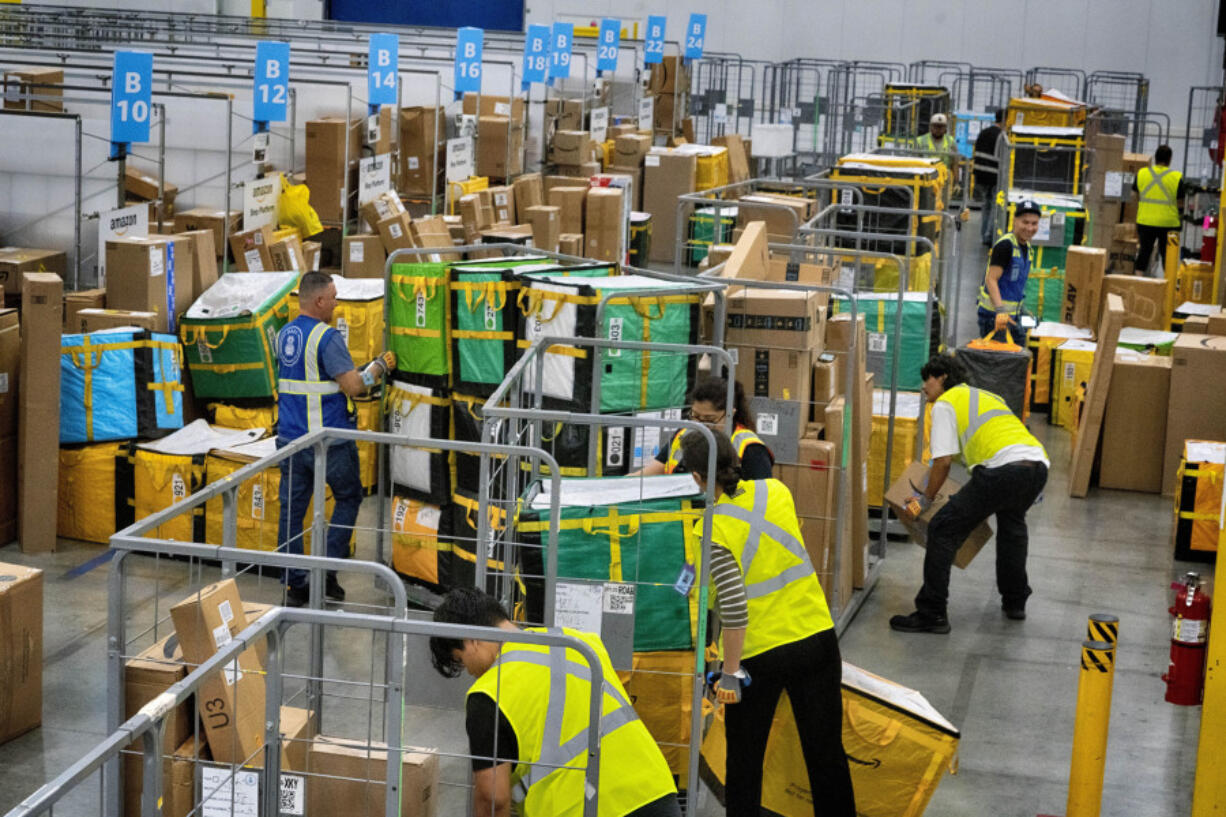 FILE - Amazon employees load packages on carts before being put on to trucks for distribution for Amazon&#039;s annual Prime Day event at an Amazon&#039;s DAX7 delivery station on July 16, 2024, in South Gate, Calif. Amazon reports earnings on Thursday, Aug. 1, 2024.