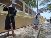 Catholic nuns sweep a sidewalk in Dili, East Timor, Monday, Aug. 12, 2024.