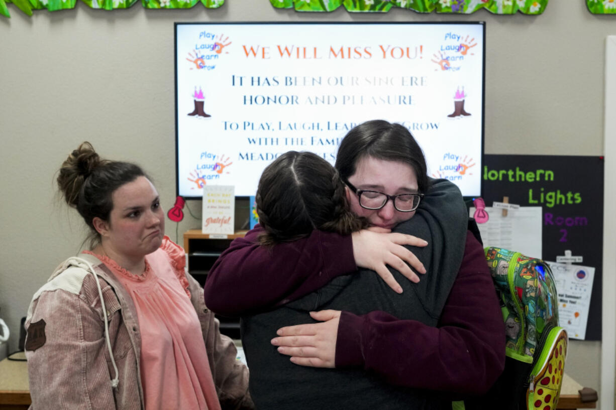 Shadows Myers, facing, hugs center receptionist Eryn Martin as Associate Educator Carrie McClure, left, looks on while they say their goodbyes following the last day of school at the Meadow Lakes CCS Early Learning, a Head Start center, Wednesday, May 8, 2024, in Wasilla, Alaska. To keep staff from leaving for higher-paying jobs elsewhere, even Target, the regional Head Start group decided it would permanently close the Meadow Lakes location at the end of the school year in an attempt to raise wages overall. About half the Meadow Lakes children and their families, many low income, hope to be granted a spot at a different Head Start center in the area, but there are few guarantees.