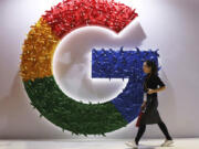 FILE - In this Nov. 5, 2018 file photo, a woman walks past the logo for Google at the China International Import Expo in Shanghai. Google is dropping plans to eliminate cookies from its Chrome web browser, making a sudden U-turn on four years of work to phase out the technology that tracks users for ad purposes.