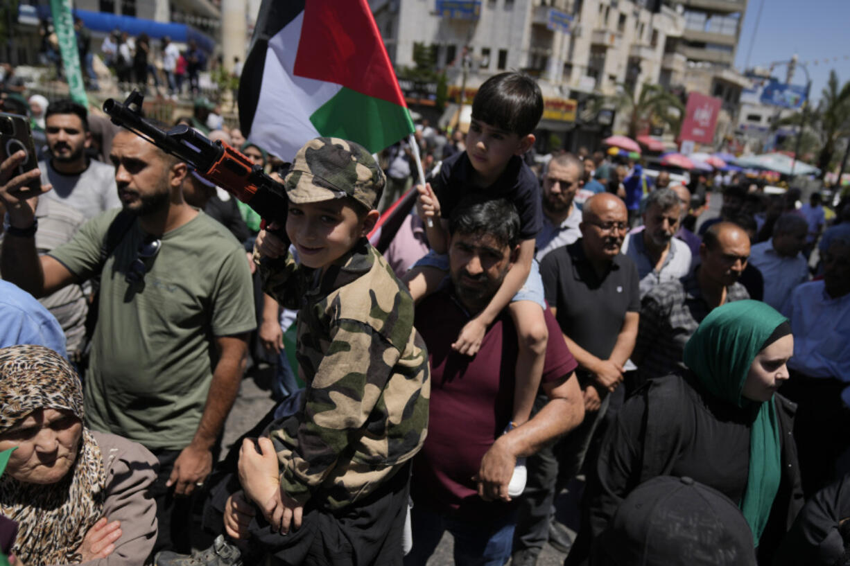 Palestinians carry children on their shoulders, one holding a toy gun and the other a Palestinian flag, as they protest the assassination of Hamas top leader Ismail Haniyeh, in the West Bank city of Ramallah, Wednesday, July 31, 2024. Two back-to-back strikes in Beirut and Tehran, both attributed to Israel and targeting high-ranking figures in Hezbollah and Hamas, have left Hezbollah and Iran in a quandary.