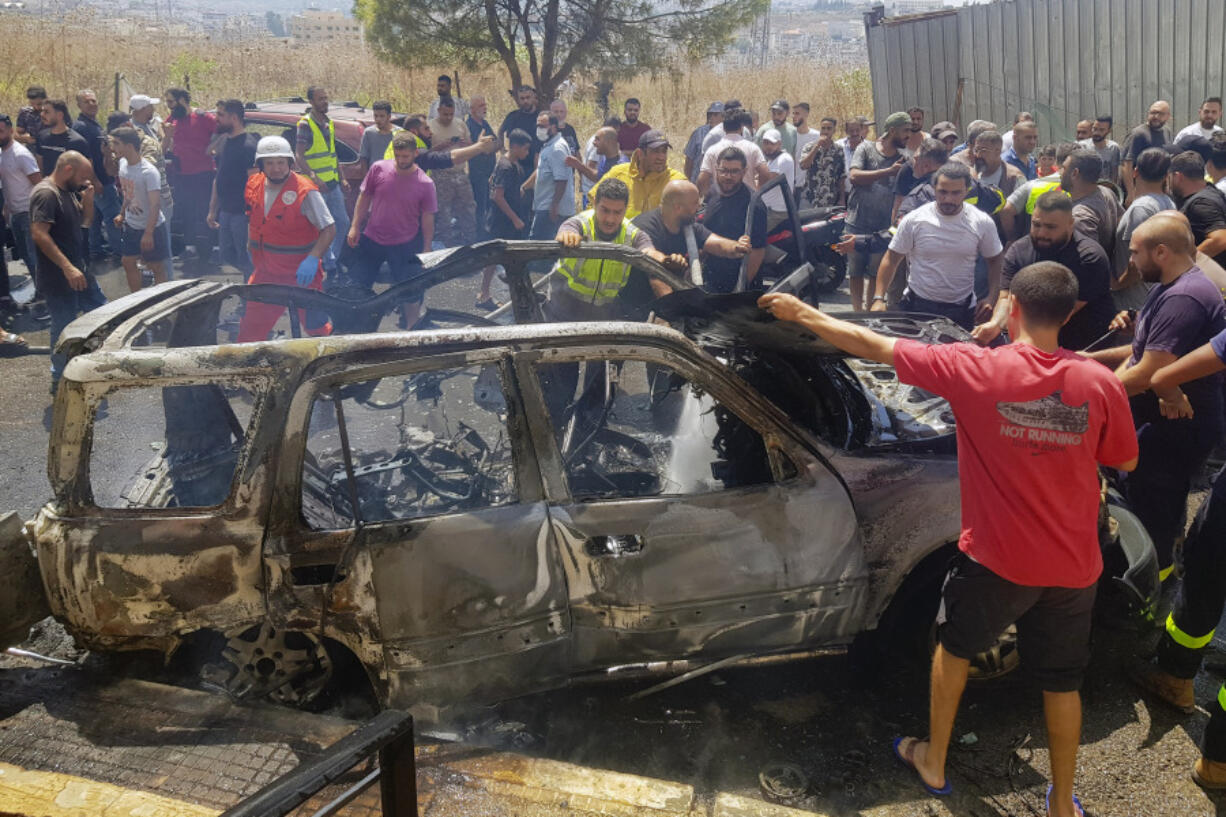 Civil Defense workers and citizens inspect the remains of a burned car that was hit by an Israeli strike in the southern port city of Sidon, Lebanon, Monday, Aug. 26, 2024.