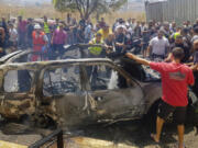 Civil Defense workers and citizens inspect the remains of a burned car that was hit by an Israeli strike in the southern port city of Sidon, Lebanon, Monday, Aug. 26, 2024.