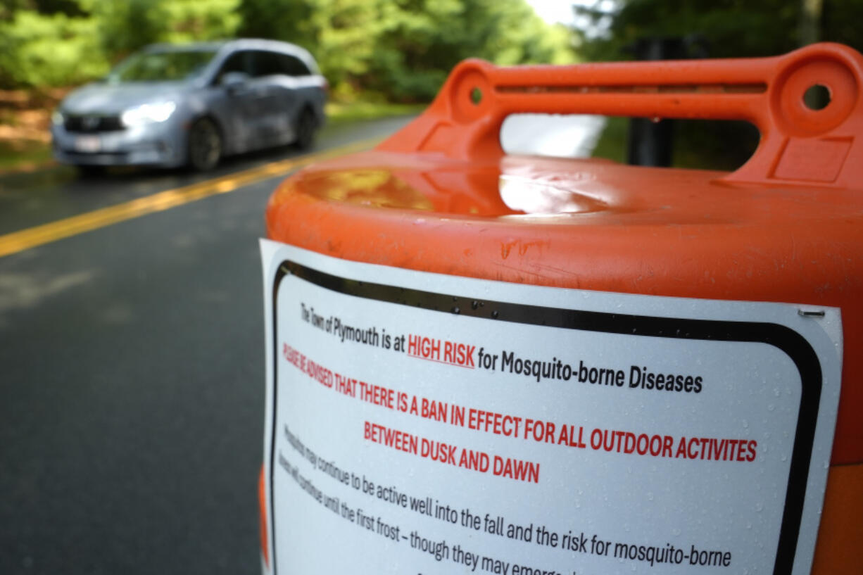 A vehicle passes a sign, Monday, Aug. 26, 2024, near an entrance to an outdoor sports complex, in Plymouth, Mass., that advises people of a ban in effect for outdoor activity between dusk and dawn due to the risk of exposure to mosquito-borne diseases.