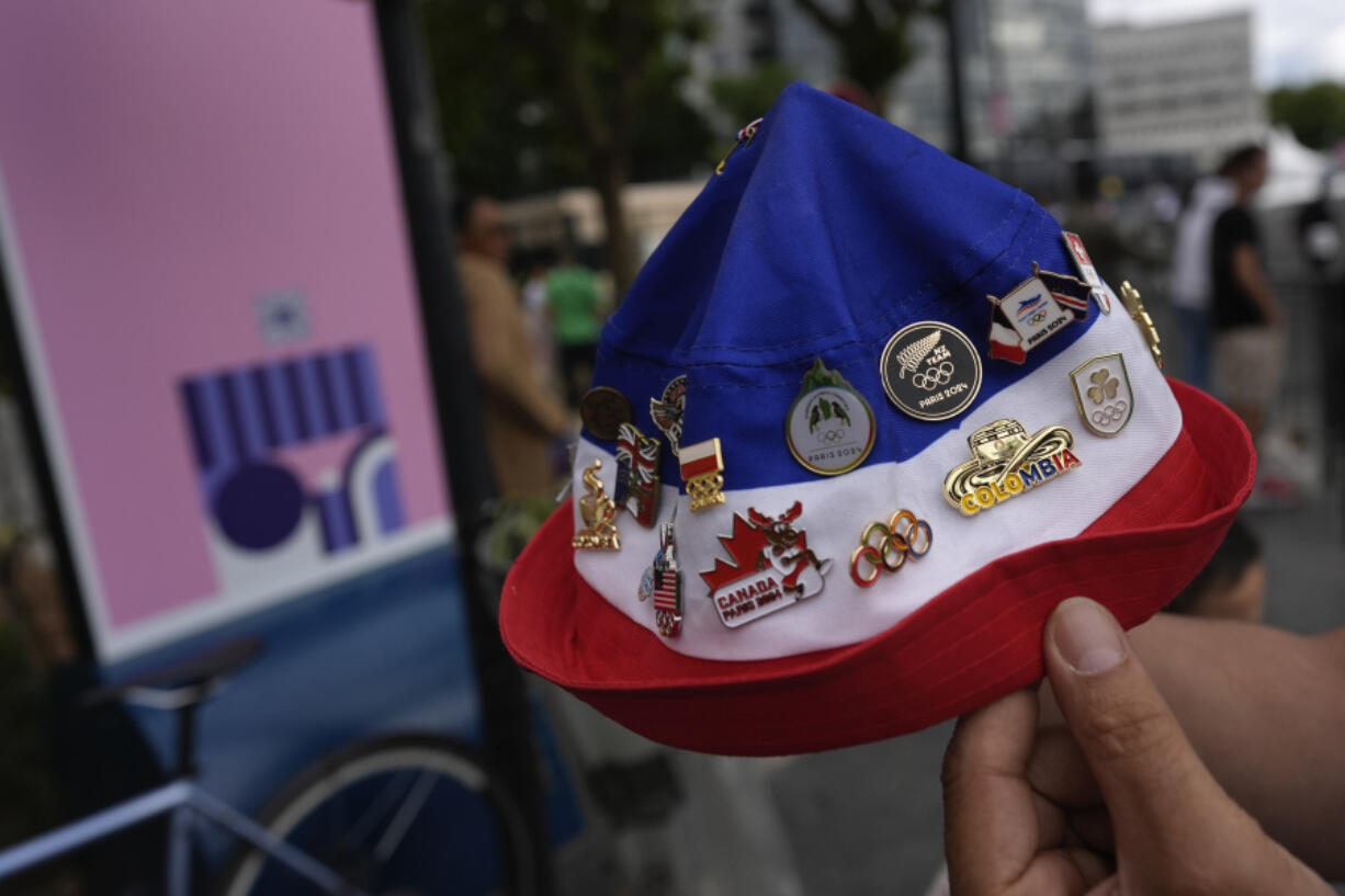 Neighborhood resident Lahlouh Wahab shows off all the 2024 Olympic pins he has been able to collect by interacting with athletes and staff from various teams outside the entrance to the Olympic Village, at the 2024 Summer Olympics on July 23 in Paris.