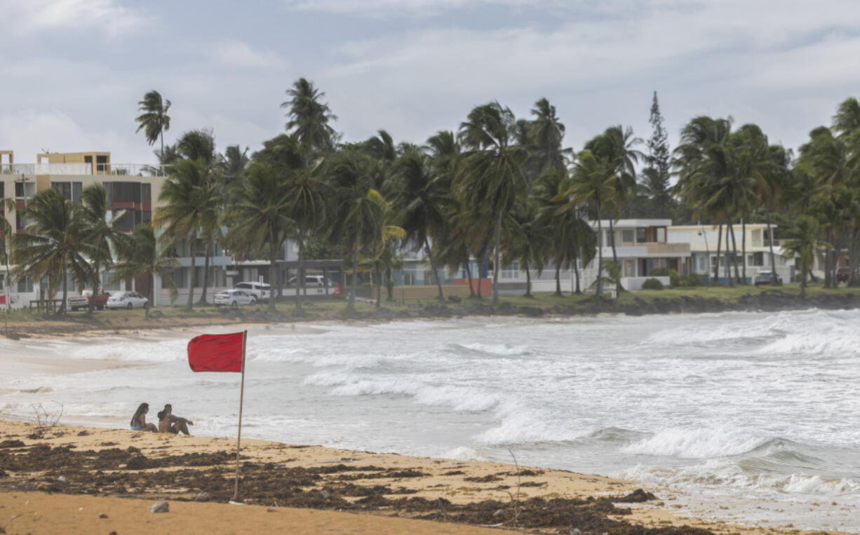 Tourists sit on La Pared beach as Tropical Storm Ernesto passes by Luquillo, Puerto Rico, Tuesday, Aug. 13, 2024.